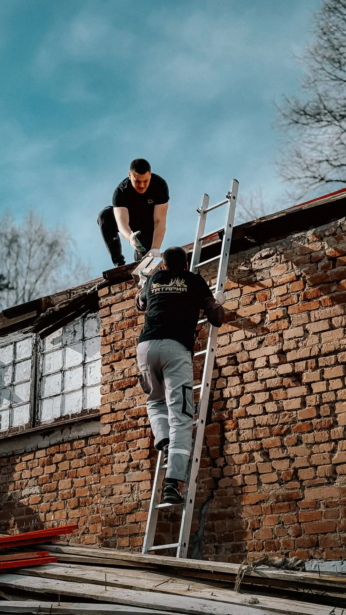 A small local roofing crew at work, one on the roof and one passing materials up a ladder